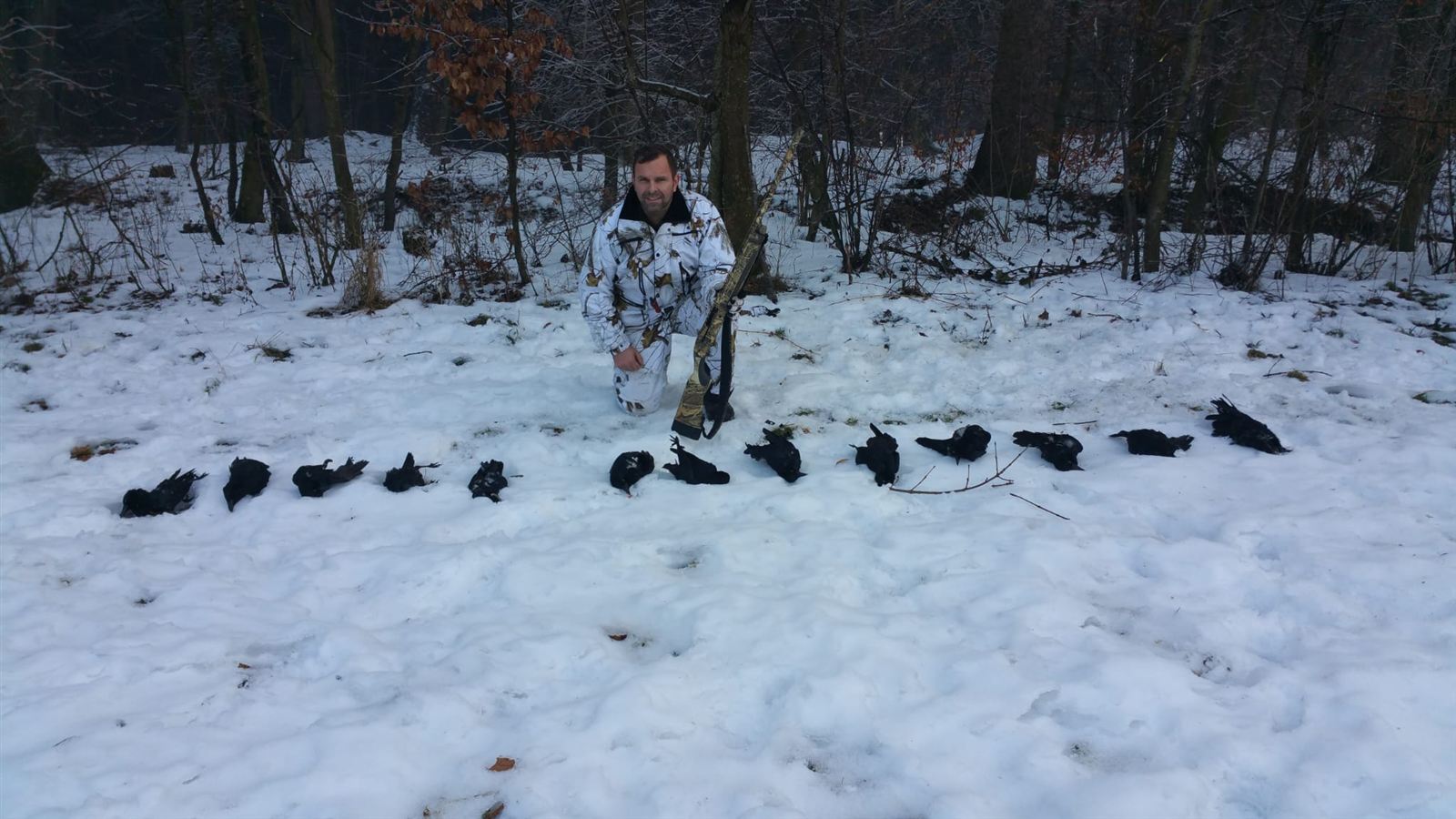 Christian Hanl in Schneetarnkleidung kniet mit Selbstladeflinte im verschneiten Wald hinter einer Reihe von 14 erlegten Krähen